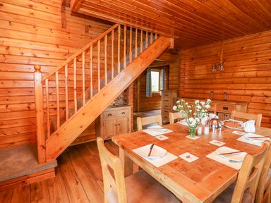 A wooden dining table set with plates utensils and flowers next to a wooden staircase in a wood-paneled room at Pines Pitch in Knighton