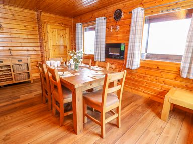 A wooden dining room with a table set for six and windows with plaid curtains at Pines Pitch in Knighton