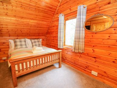 A bedroom with wooden walls a bed with plaid pillows and folded towels at Pines Pitch in Knighton