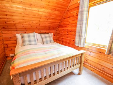 A wooden bedroom with a bed with plaid pillows and a striped blanket at Pines Pitch in Knighton