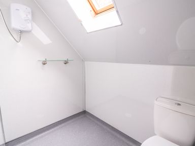 A small bathroom with a toilet, a shower unit, a glass shelf, and a skylight window at Pines Pitch in Knighton