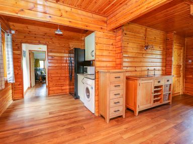 A kitchen area with wooden cabinets a washing machine refrigerator and wooden drawers at Pines Pitch in Knighton