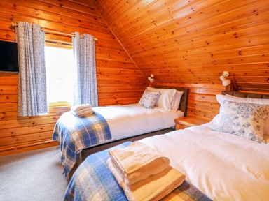 A bedroom with two single beds wooden walls window with curtains and folded towels at Pines Pitch in Knighton