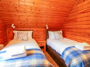 A bedroom with two single beds with white bedding and blue plaid blankets in a wooden cabin at Pines Pitch in Knighton