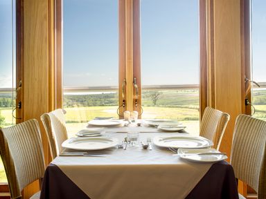A dining table set for six with plates and cutlery facing large windows with a view of fields and trees at Ullswater 29 in Penrith