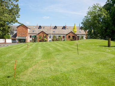 A putting green with flags and markers in front of a building with multiple windows and flags at Ullswater 29 in Penrith