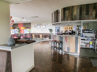 An indoor bar area with wooden stools and a curved wooden counter next to a seating area with tables and chairs at Ullswater 29 Penrith