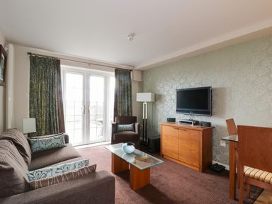 A living room with a sofa armchair glass coffee table and TV on a cabinet at Ullswater 29 in Penrith