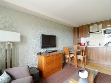 A living area with a sofa lamp television wooden cabinet dining table chairs and a kitchen with wooden cabinets at Ullswater 29 in Penrith