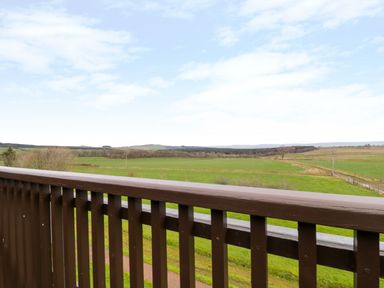 A wooden balcony railing with green fields and trees in the background at Ullswater 29 in Penrith