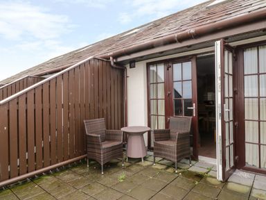 An outdoor patio area with two wicker chairs and a small round table outside double doors at Ullswater 29 Penrith