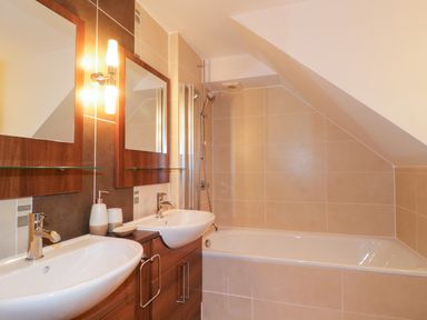 A bathroom with double sinks wooden cabinets a bathtub and shower at Ullswater 29 in Penrith