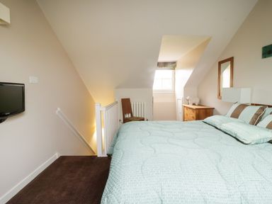 A bedroom with a bed a chair a dresser a window and a small wall mounted television at Ullswater 29 in Penrith