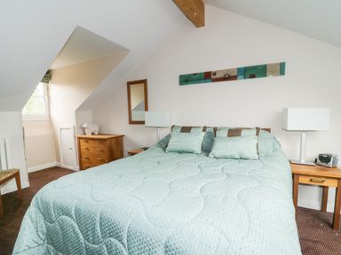 A bedroom with a bed covered by a green cover and pillows two bedside tables with lamps and a wooden chest of drawers and a window at Ullswater 29 in Penrith