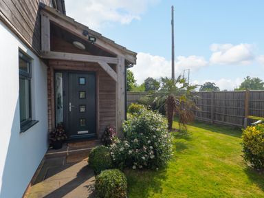 Front door entrance with plants and bushes beside a lawn with a wooden fence at Longmynd in Gloucester