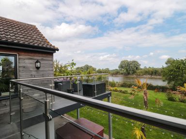 A balcony with glass railing overlooking a garden and a river at Longmynd in Gloucester