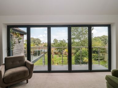 A room with glass doors opening to a balcony with a metal railing and a view of trees and a garden at Longmynd in Gloucester