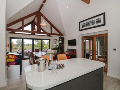 A dining area with a large wooden table and chairs under a vaulted ceiling with wooden beams and glass doors leading outside at Longmynd in Gloucester