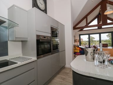A kitchen with gray cabinets built in oven and microwave and a countertop with champagne bottle and glasses at Longmynd in Gloucester