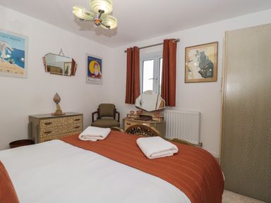 A bedroom with a bed with orange bedding and white towels a dresser a chair curtains and framed pictures at Longmynd in Gloucester