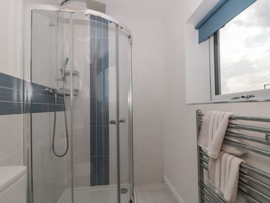 A bathroom with a glass shower enclosure a shower head and a towel rack with towels near a window at Longmynd in Gloucester