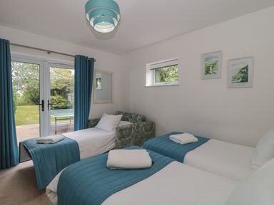 A bedroom with two single beds and a daybed with teal covers white pillows blue curtains and glass doors opening to a garden at Longmynd in Gloucester
