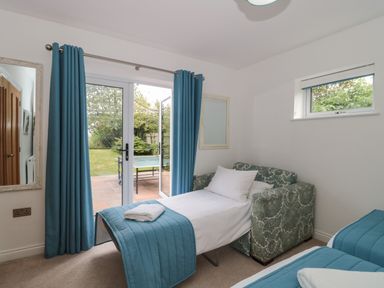 A small bedroom with a sofa bed, blue curtains, a window, and glass doors opening to a garden at Longmynd in Gloucester