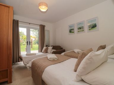 A bedroom with three single beds brown cushions and throws a brown armchair and glass doors leading to a garden at Longmynd in Gloucester