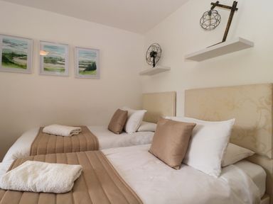 A bedroom with two single beds brown throws white pillows and two wall shelves with decorative items at Longmynd in Gloucester
