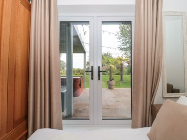 A bedroom with curtains and glass doors opening to a patio with plants and string lights at Longmynd in Gloucester