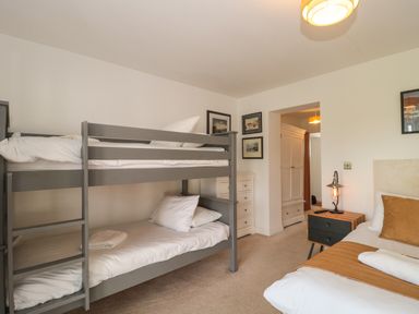 A bedroom with a gray bunk bed white drawers a bedside table and a bed at Longmynd in Gloucester
