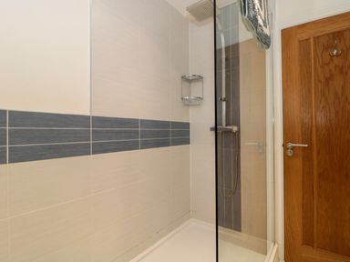 A shower area with tiled walls a glass door a rain shower head and a wooden door in a bathroom at Longmynd in Gloucester