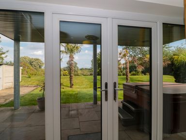 View through glass doors of a patio with hot tub and garden with palm trees at Longmynd in Gloucester