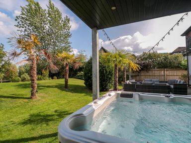 An outdoor area with a hot tub palm trees string lights and wicker patio furniture at Longmynd in Gloucester