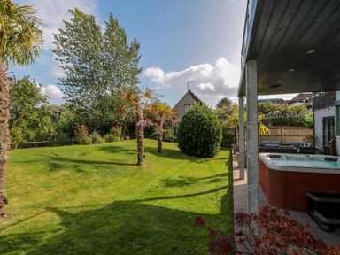 A backyard with a hot tub under a covered patio and palm trees on grass at Longmynd in Gloucester