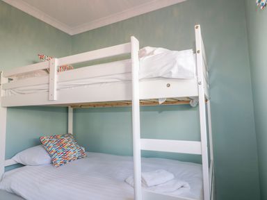 A bedroom with a white bunk bed and pillows against a green wall at Bayview in Mevagissey