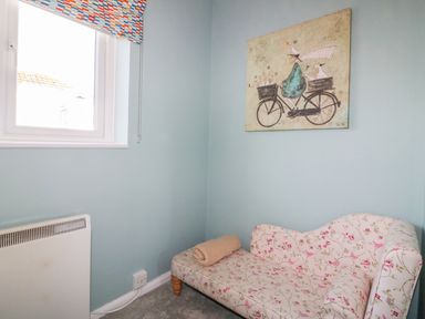 A small room with a window and a floral patterned chaise lounge and a painting on the wall at Bayview in Mevagissey