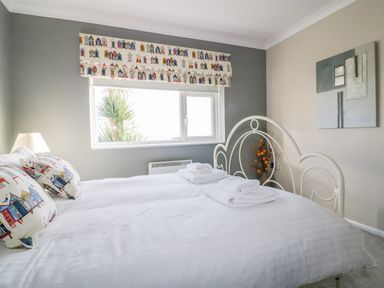 A bedroom with a white metal bed frame pillows with house patterns window with matching blinds and folded towels on the bed at Bayview in Mevagissey