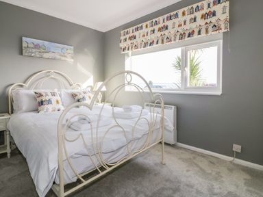 A bedroom with a white metal bed frame, white bedding, two small nightstands, a window with patterned blinds, and a painting on the wall at Bayview in Mevagissey