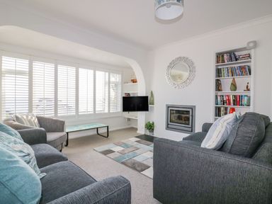 A living room with sofas a coffee table a rug a built in bookshelf and a wall mounted tv at Bayview in Mevagissey