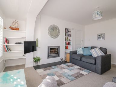 A living room with a grey sofa a rug and a fireplace at Bayview in Mevagissey