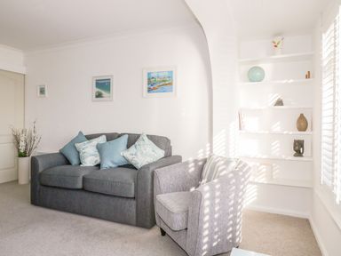 A living room with a gray sofa and armchair with cushions and white shelves with decorations at Bayview in Mevagissey