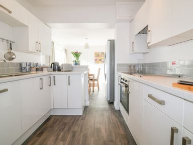 A kitchen with white cabinets a gray countertop a black kettle a toaster and flowers on the counter at Bayview in Mevagissey
