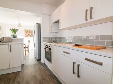 A kitchen with white cabinets a cutting board an oven and a stainless steel refrigerator at Bayview in Mevagissey
