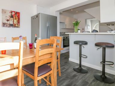 A kitchen and dining area with wooden chairs around a table a double door fridge and bar stools at Bayview in Mevagissey