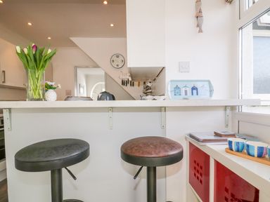 A kitchen counter with two bar stools a vase with flowers and kitchen utensils at Bayview in Mevagissey