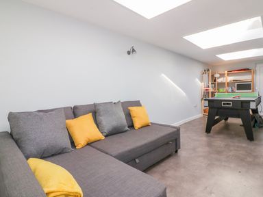 A room with a gray sectional sofa with yellow and gray cushions a black ping pong table and wooden shelves at Bayview in Mevagissey