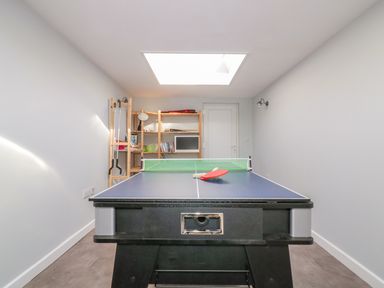 A narrow room with a ping pong table at the center and shelves with books and equipment at the back Bayview Mevagissey