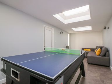 A room with a ping pong table and a gray sectional sofa with yellow cushions at Bayview in Mevagissey