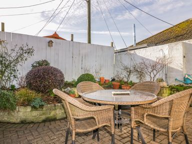 An outdoor patio area with wicker chairs around a round glass table and potted plants along a white wooden fence at Bayview in Mevagissey